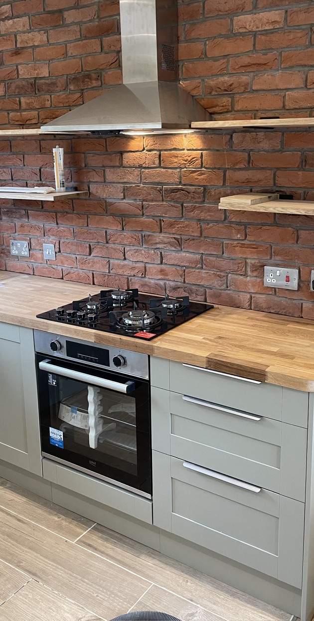 Completed kitchen with grey cabinets, timber worktop and brick splashback